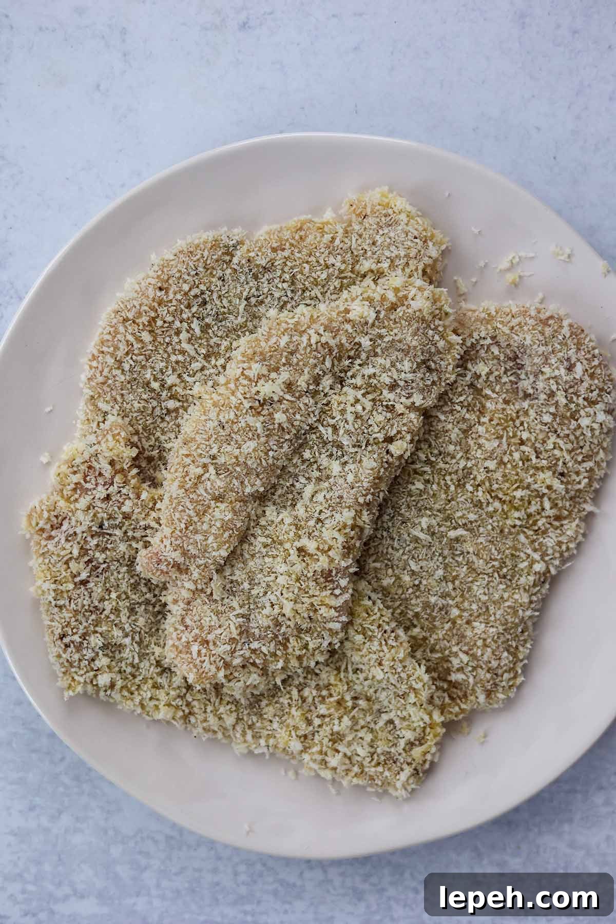 four raw chicken breasts coated in panko breadcrumbs.