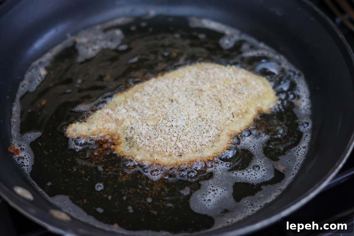 chicken milanese frying in a skillet with oil.