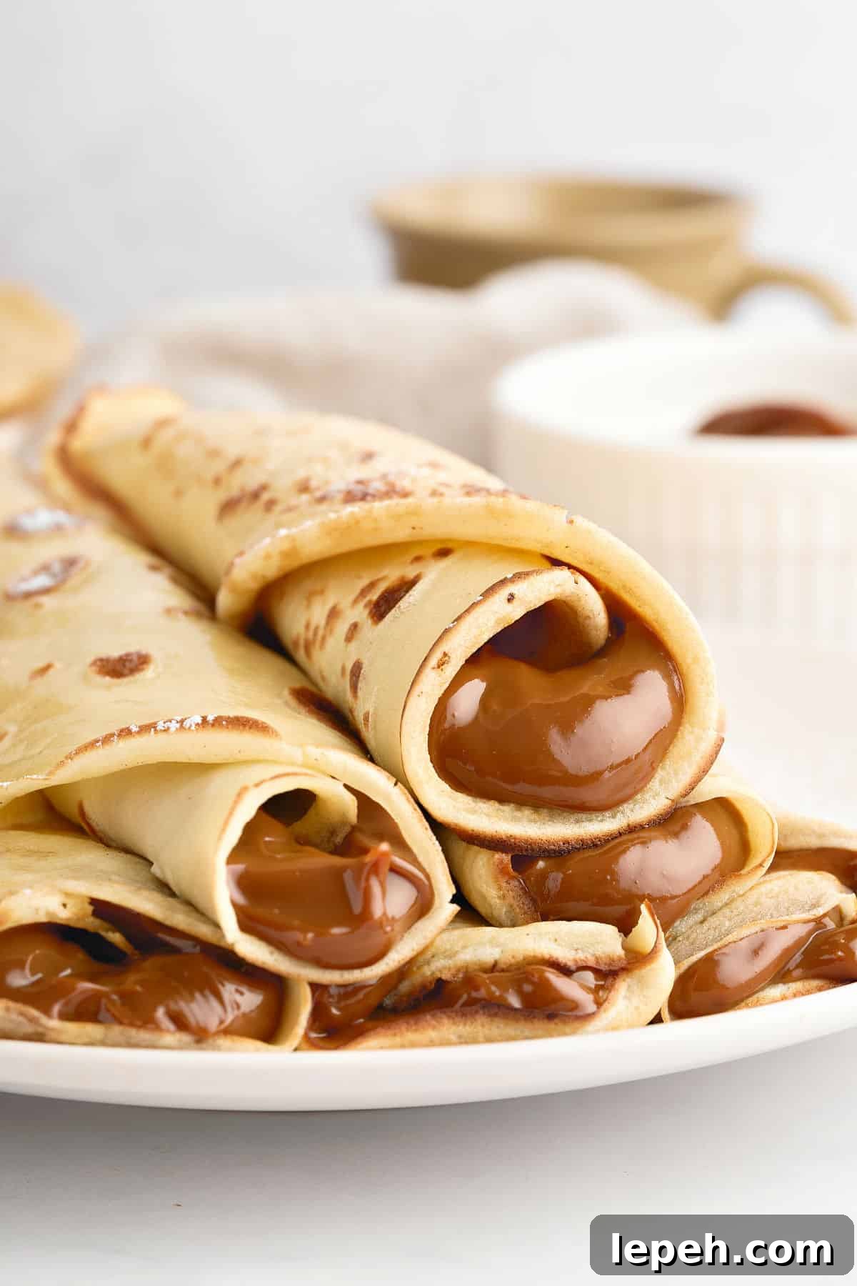 Pile of rolled dulce de leche thin pancakes on a white plate. White background. 