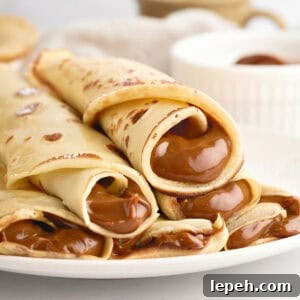 Rolled dulce de leche crepes on a white plate. White background.