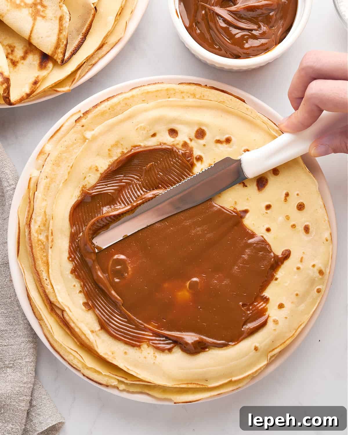 Spreading dulce de leche on thin recpes. White background. Top view.
