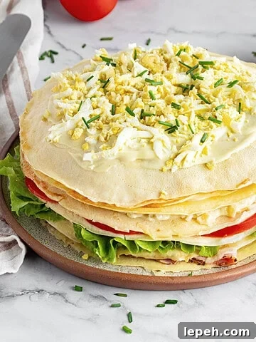 Whole savory crepe cake on a plate. White marbled surface, bowl with mayo.