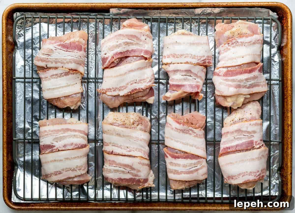 boneless skinless chicken thighs wrapped in bacon on wire rack before baking.