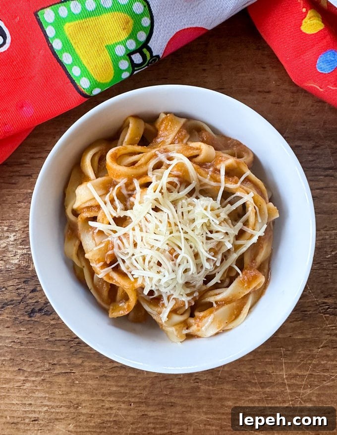 Slow Cooker Ten Hidden Veggie Sauce mixed with cooked linguine in a white bowl and garnished with a sprinkling of finely grated cheese.