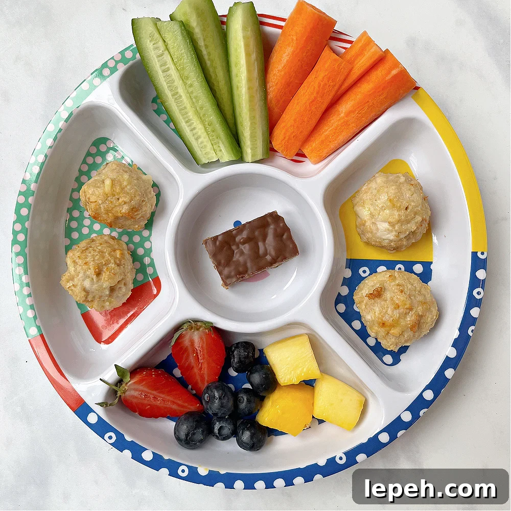 Cheesy Chicken Meatballs served in a  colourful divided kids plate from Pick Plates with chopped veggies, fruit and a chocolate flapjack.