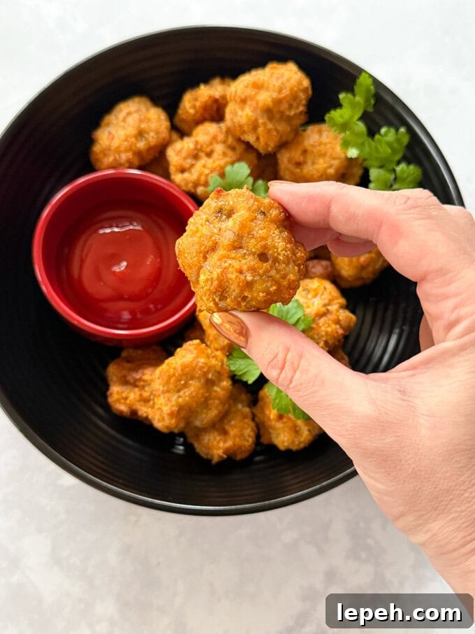 Chicken nuggets served in a large,round black bowl. with a separate small red bowl filled with ketchup for dipping.