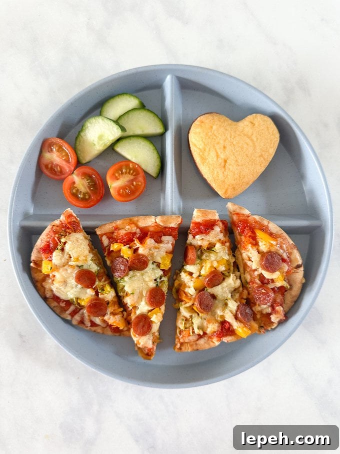 Pitta Pizza Bread With Hidden Veggies served on a blue divided plate with a side serving of cucumber and cherry tomatoes and a mini heart shaped cake.