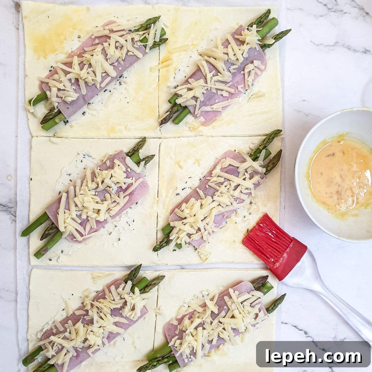 Beaten egg being brushed onto the corners of the ham and asparagus pastry squares.