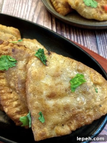 Crispy cheese and sweetcorn samosas on a black plate.