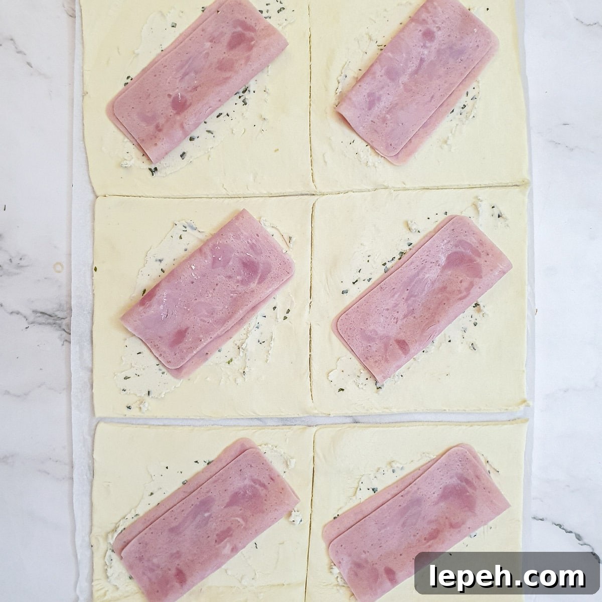 Slices of ham on top of the puff pastry squares.