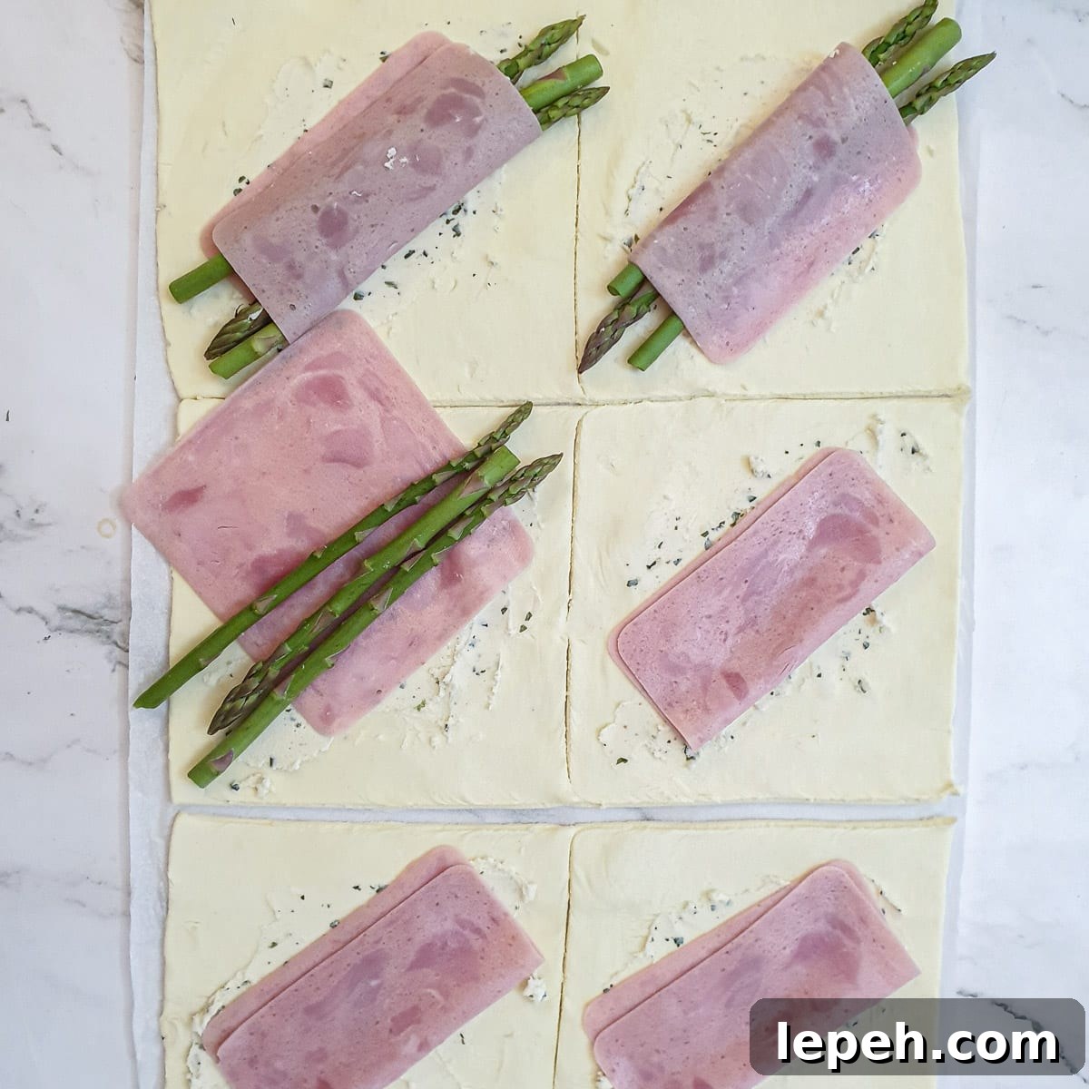 Asparagus spears being added to the ham on the puff pastry squares.