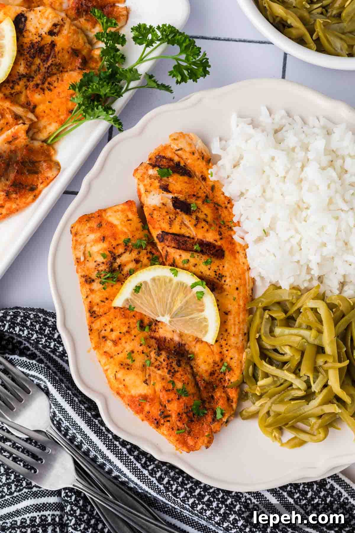 Grilled tilapia on a plate with white rice and green beans