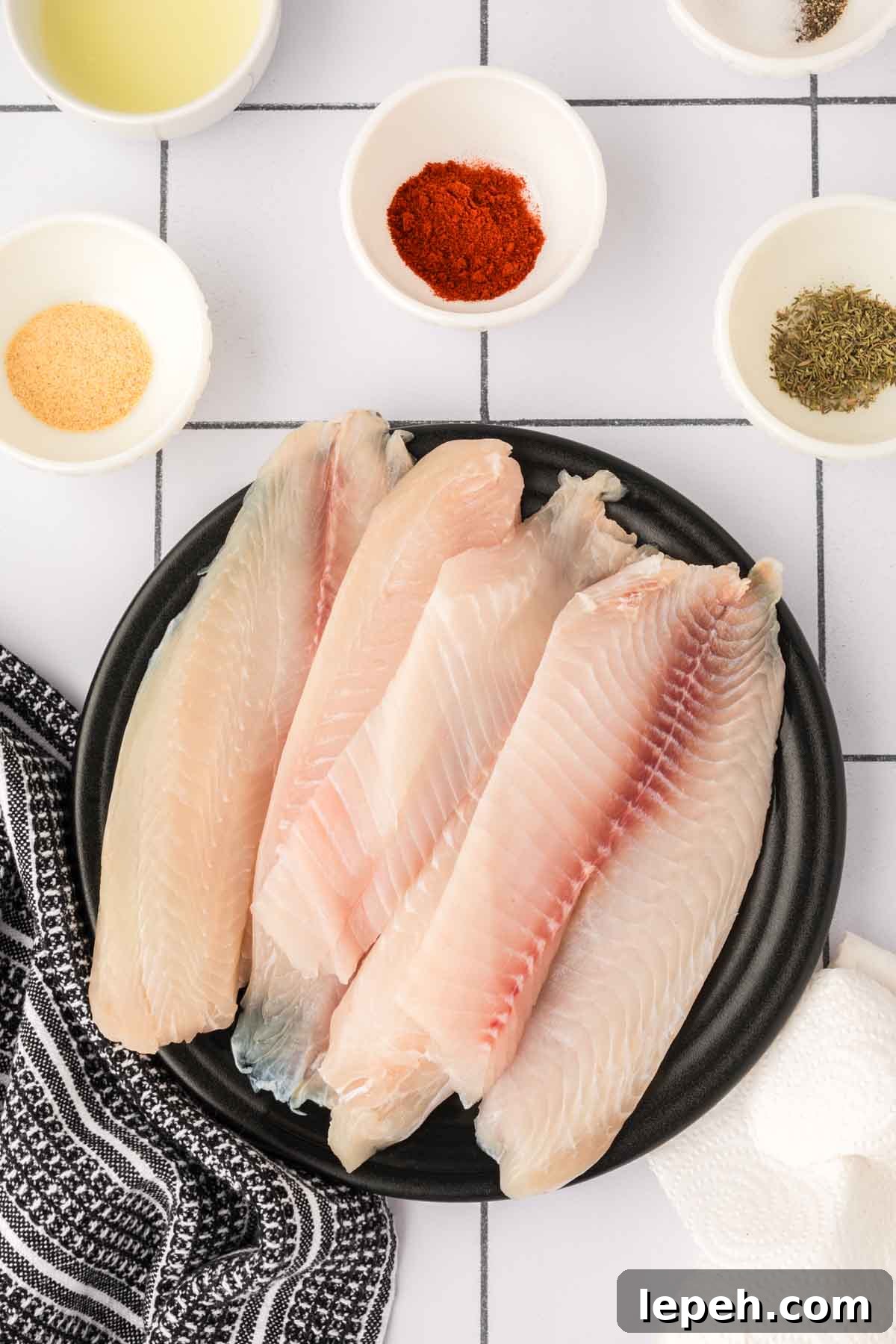 Uncooked tilapia fillets on a plate with bowls of seasoning on the side