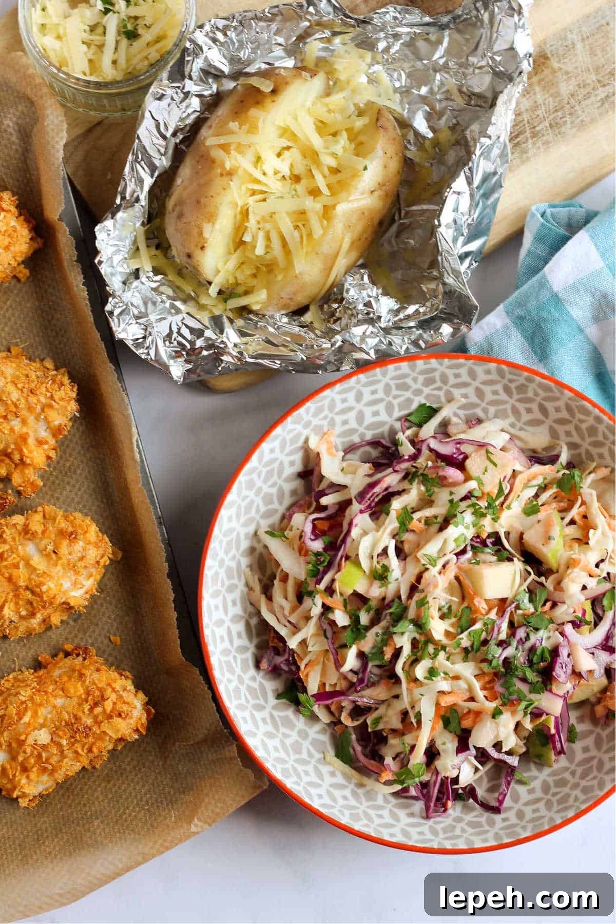 Apple coleslaw in a bowl with a baked potato and cornflake chicken nuggets