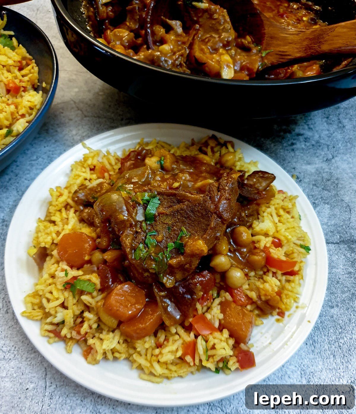 A white plate of Moroccan rice topped with lamb tagine.