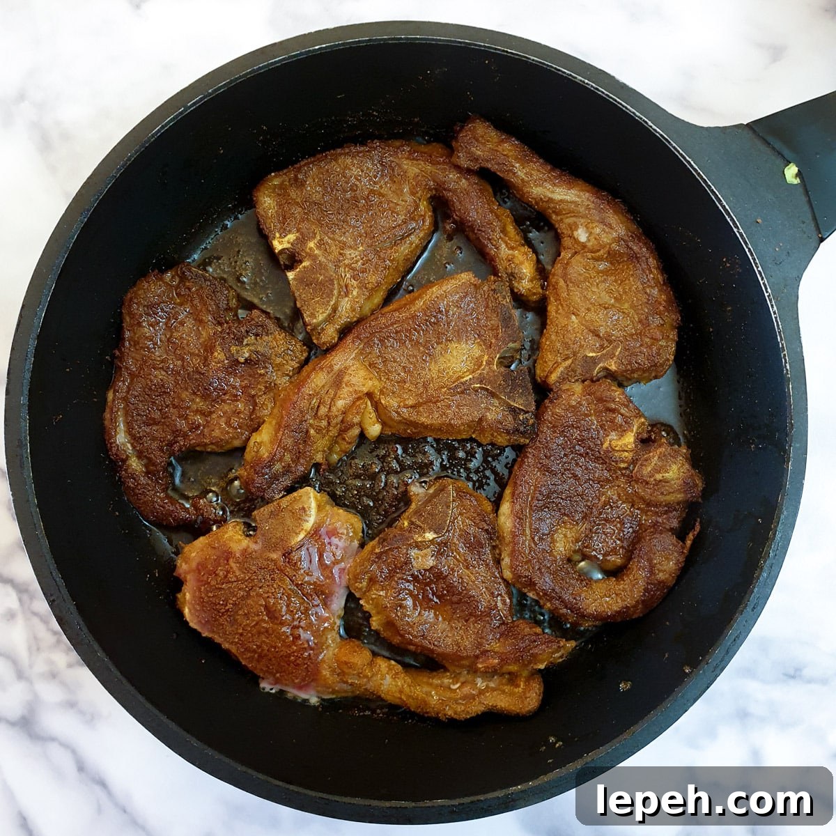 Spice coated lamb chops in a frying pan.