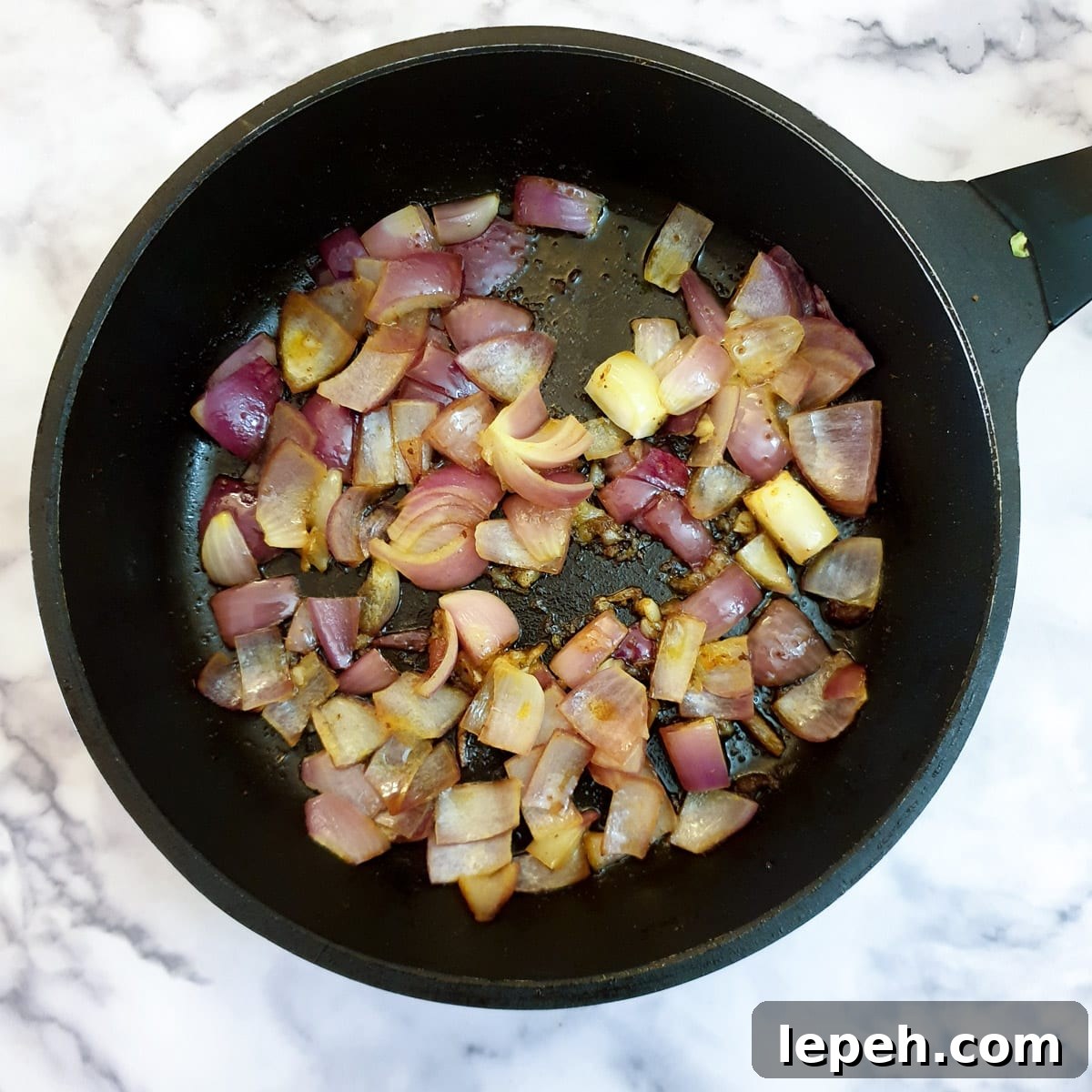 Onions and garlic softening in a frying pan.