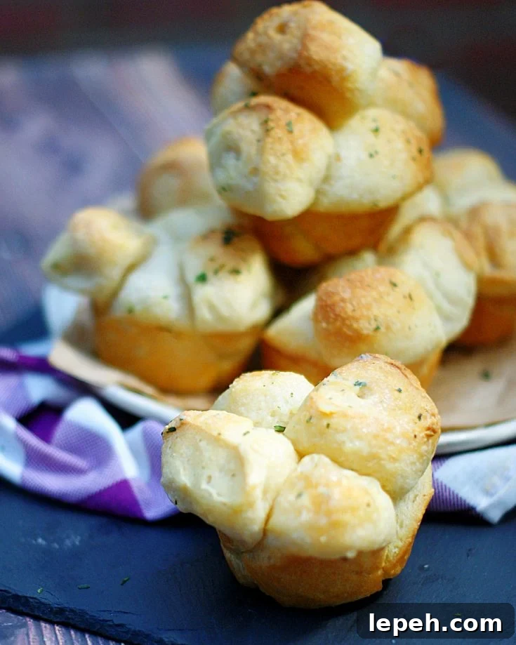 A close up of a shortcut pull apart roll with a plate full of buttery rolls behind it.