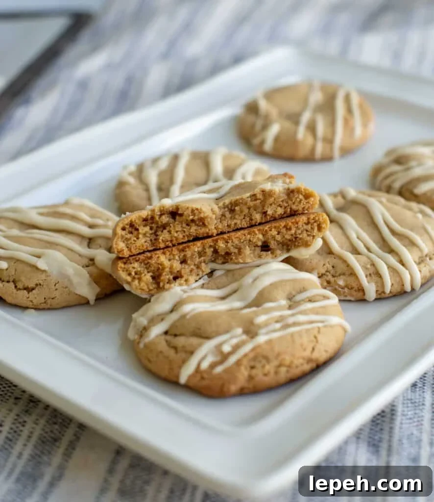 Brown sugar sourdough maple cookie broken in half to show the chewy middle and sitting on a plate on top of other cookies.