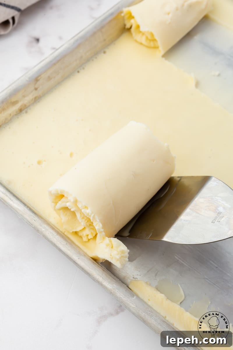 a spatula scraping ice cream rolls off of a sheet pan.