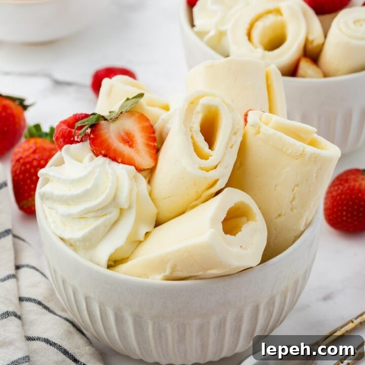 a white bowl filled with rolls of vanilla ice cream, topped with whipped cream and fresh berries. There are two spoons next to the bowl.