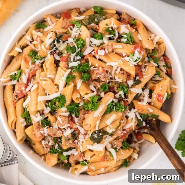 Instant Pot pasta with sausage, spinach, tomatoes, in white bowl.