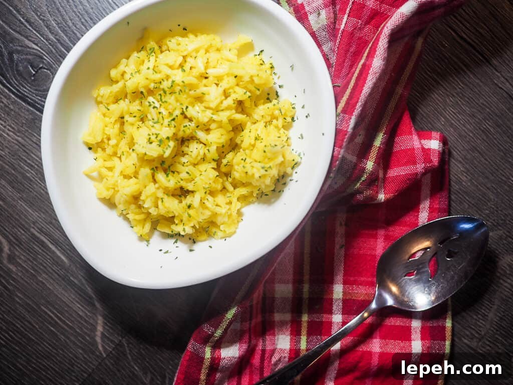 A white bowl with rice pilaf and a silver spoon and red plain napkin.