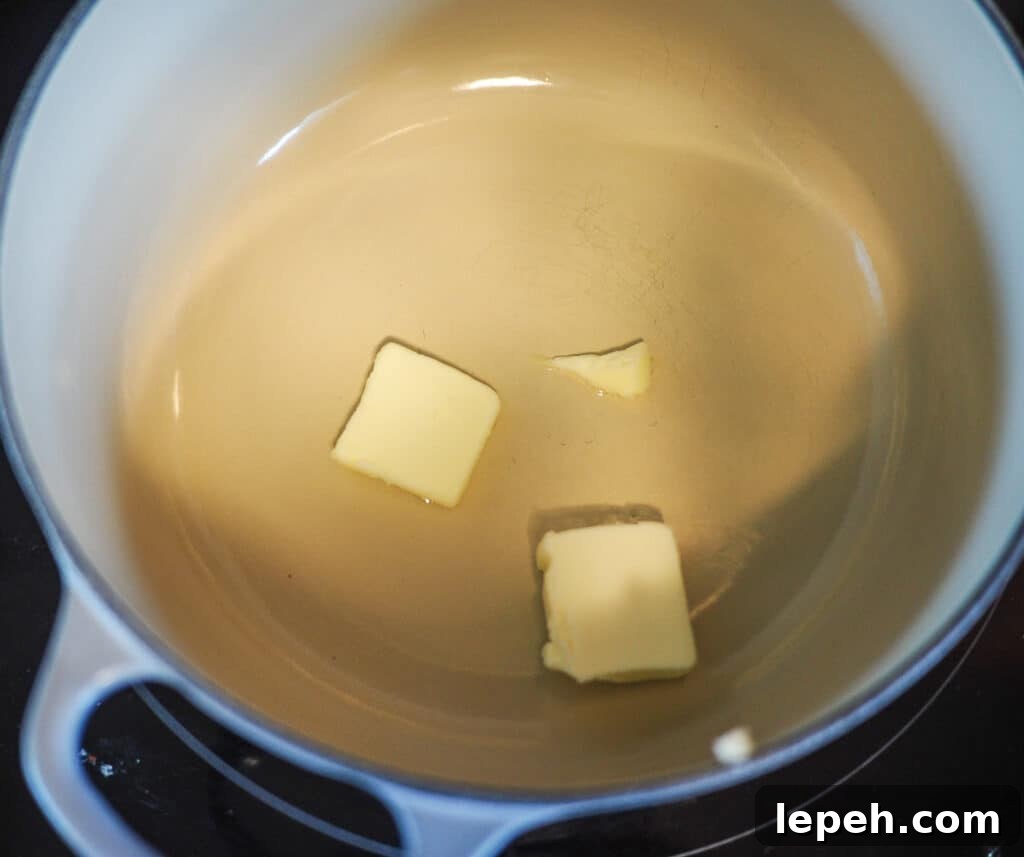 Squares of butter melting in a small, white and gray pot.