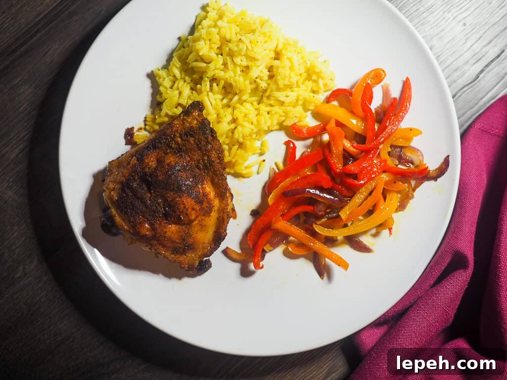A white plate with a crispy chicken thigh, sautéed bell peppers, and rice pilaf.