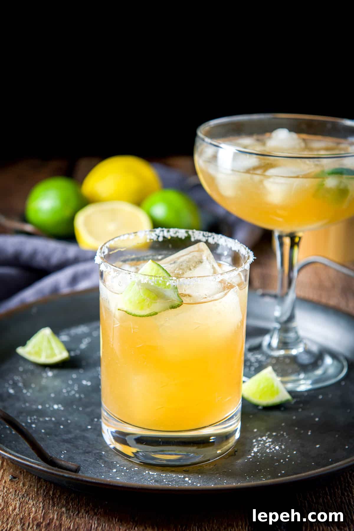 A metal tray with lime and salt strewn and two glasses with margaritas in them