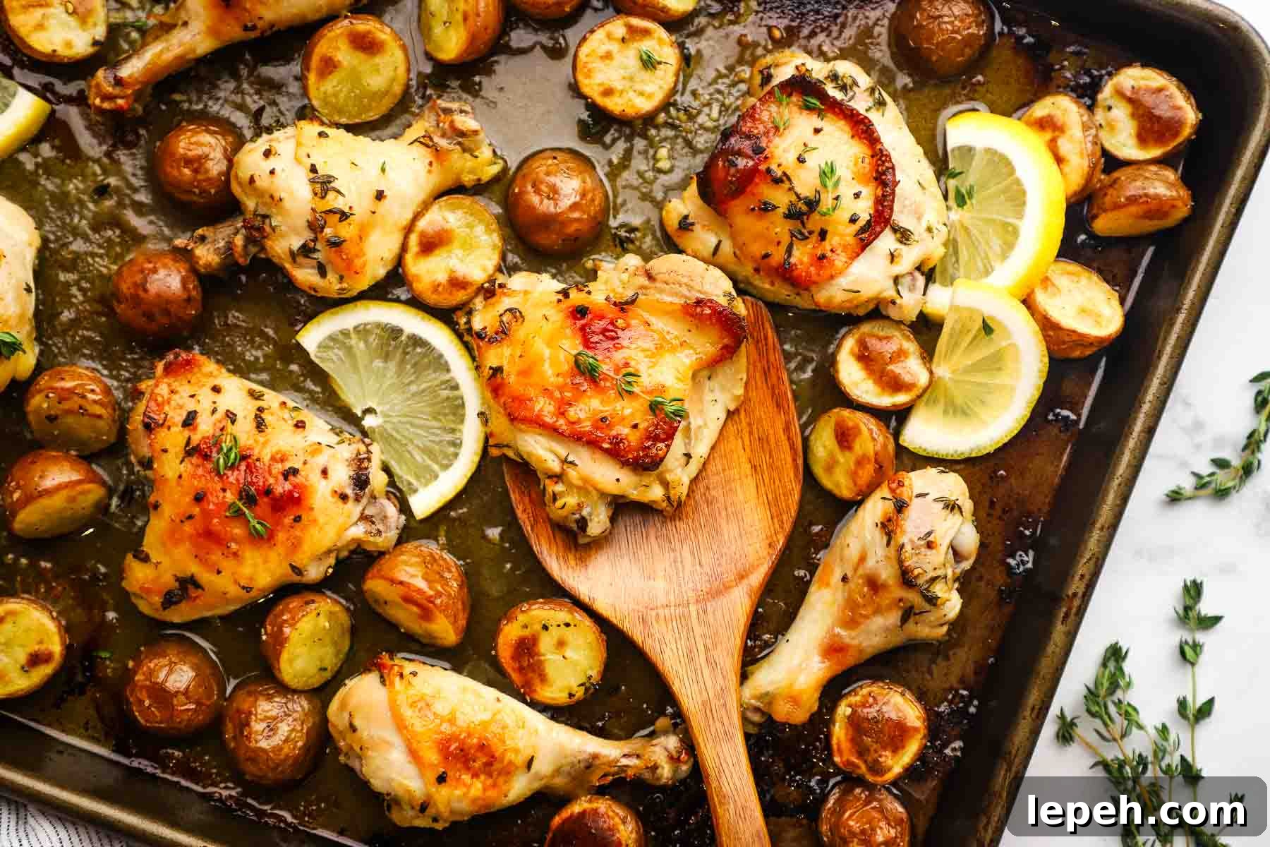 Roasted chicken parts and potatoes on a sheet pan with a wooden spatula.