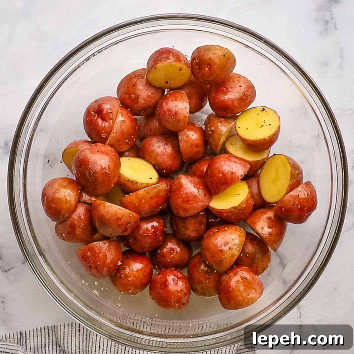 baby potatoes in a bowl cut in halves tossed with olive oil, salt, and black pepper