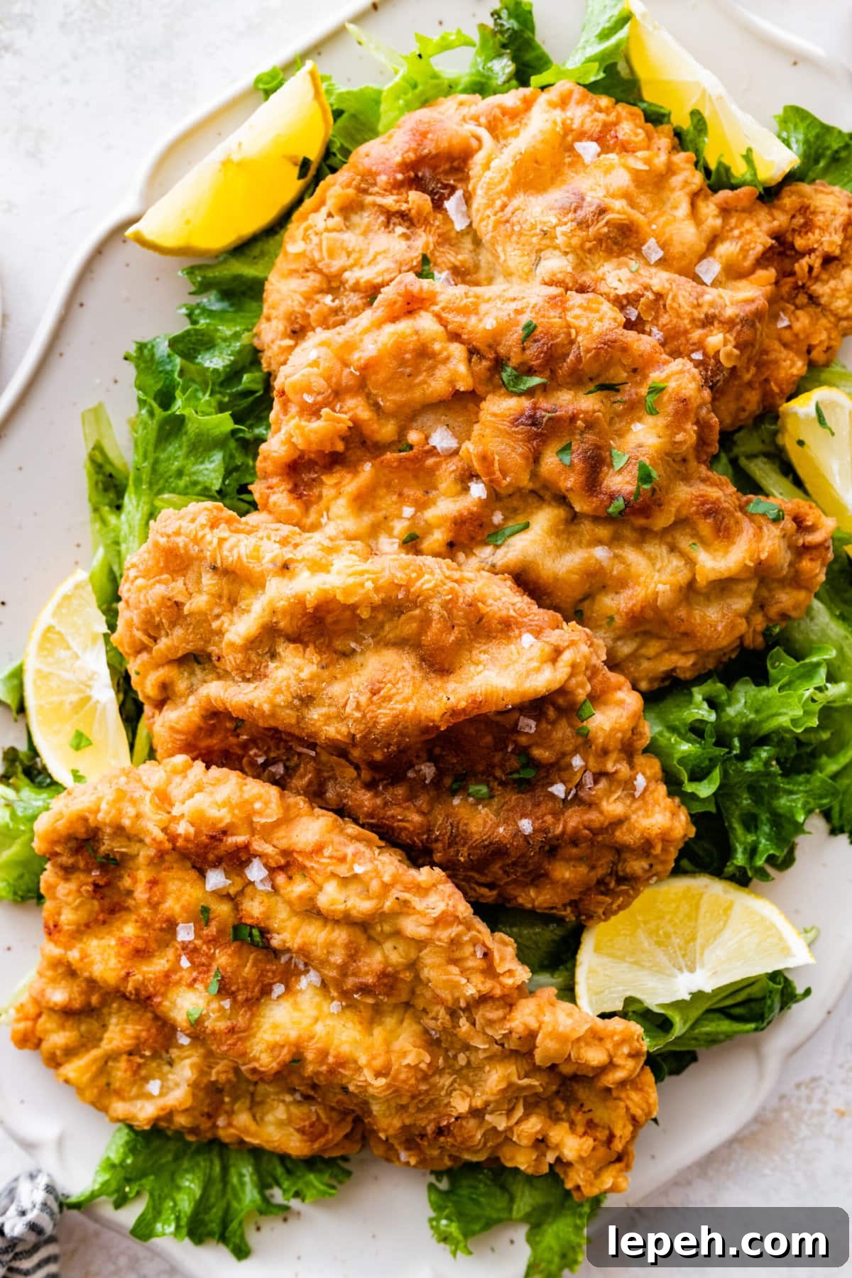 Crispy fried pork chops on a plate with salad and lemon wedges.