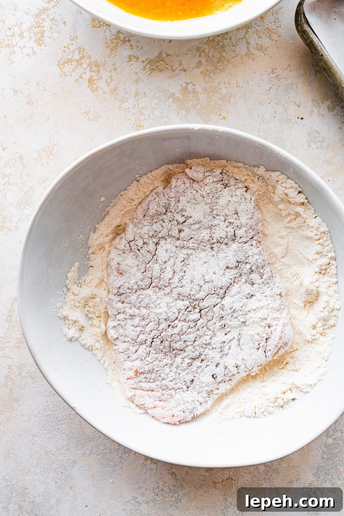 Pork chop in a bowl of flour coated on both sides.
