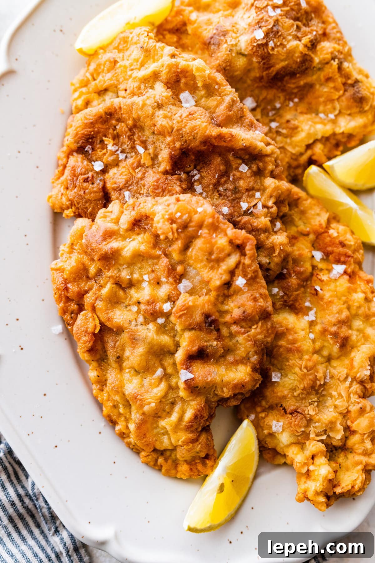 Breaded fried pork chops on a platter sprinkled with flaked salt and lemons.
