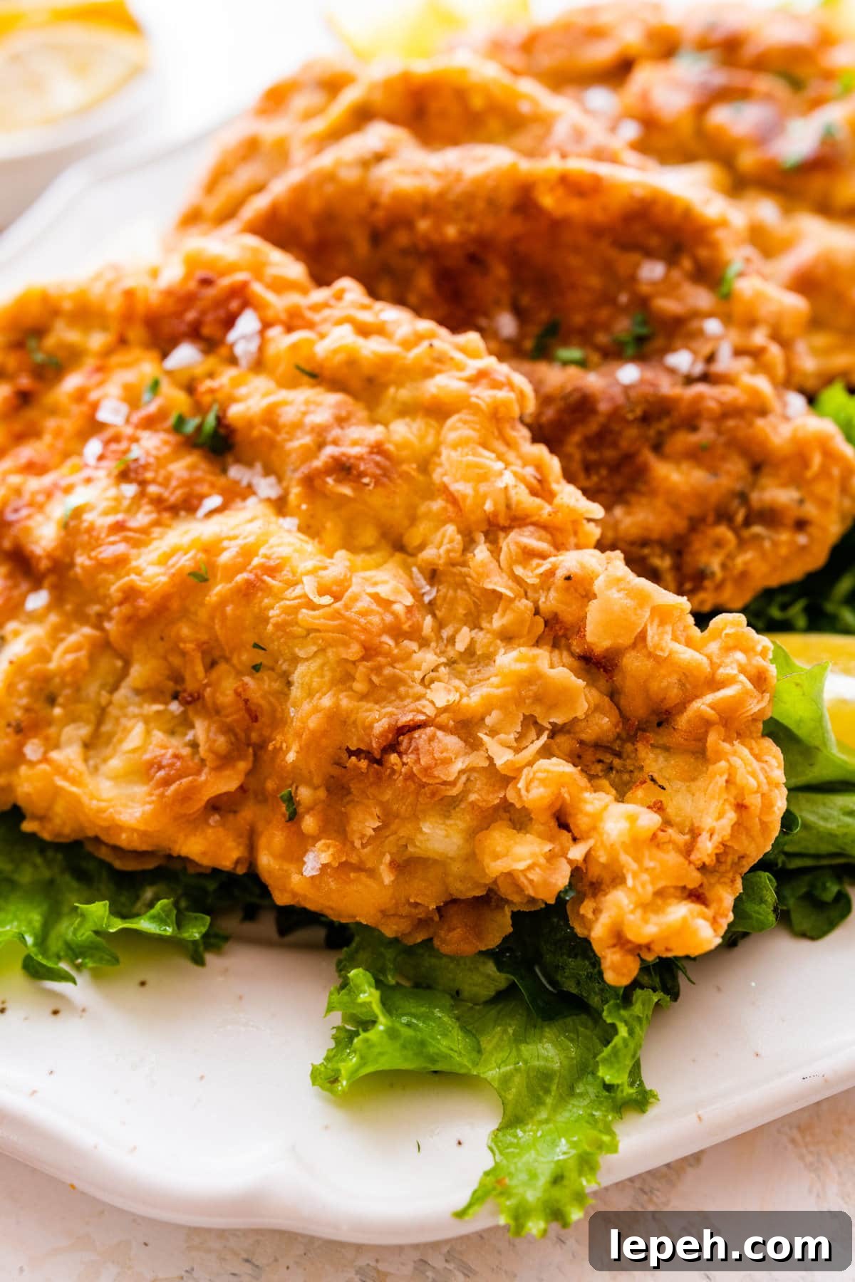 Fried pork chops on a plate with lettuce underneath and lemon wedges on the side.