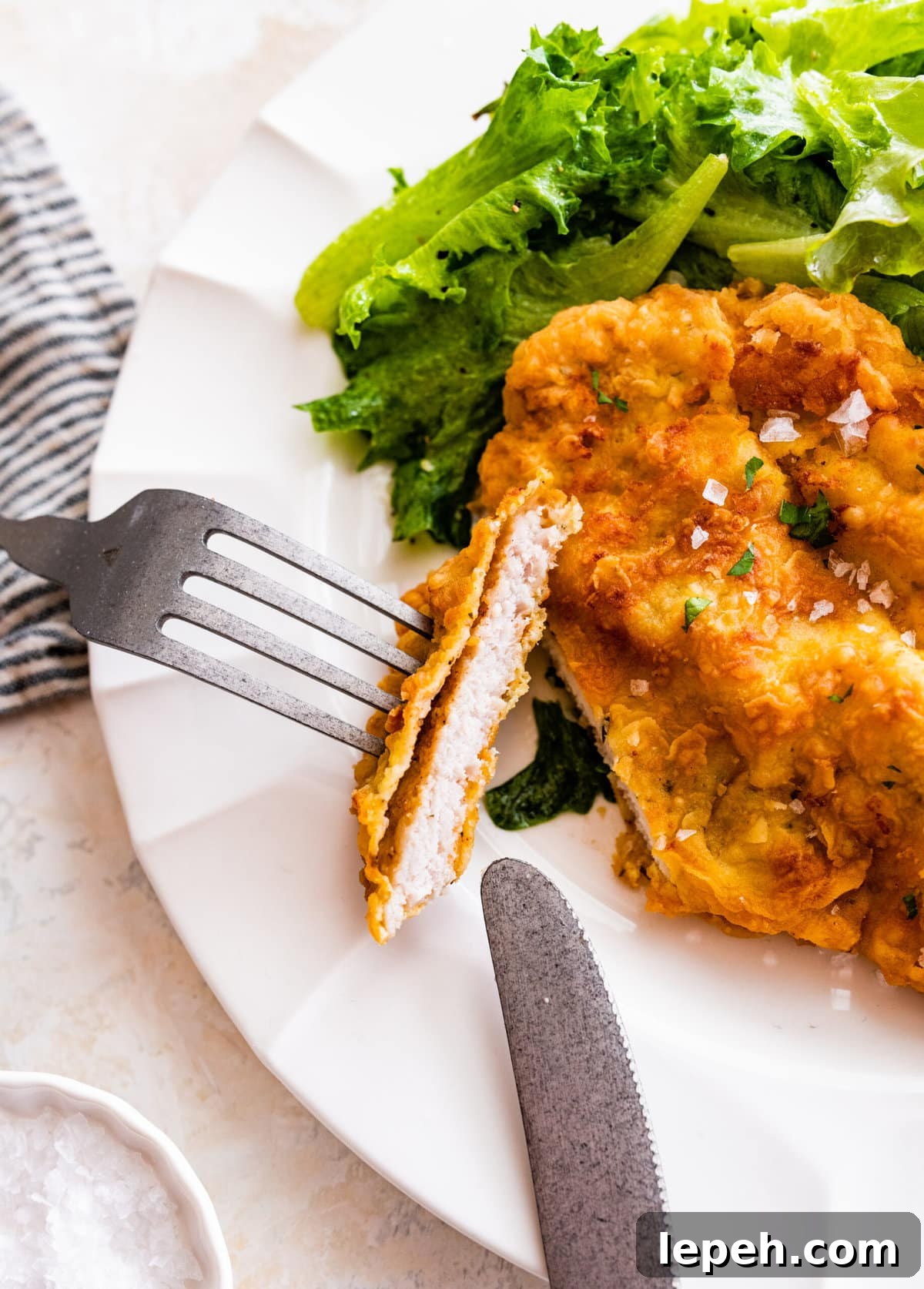 Plated crispy pork chop with a bite taken out and side of salad.