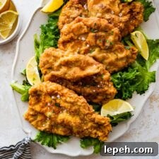 Crispy fried pork chops on a platter with lemon wedges and greens.