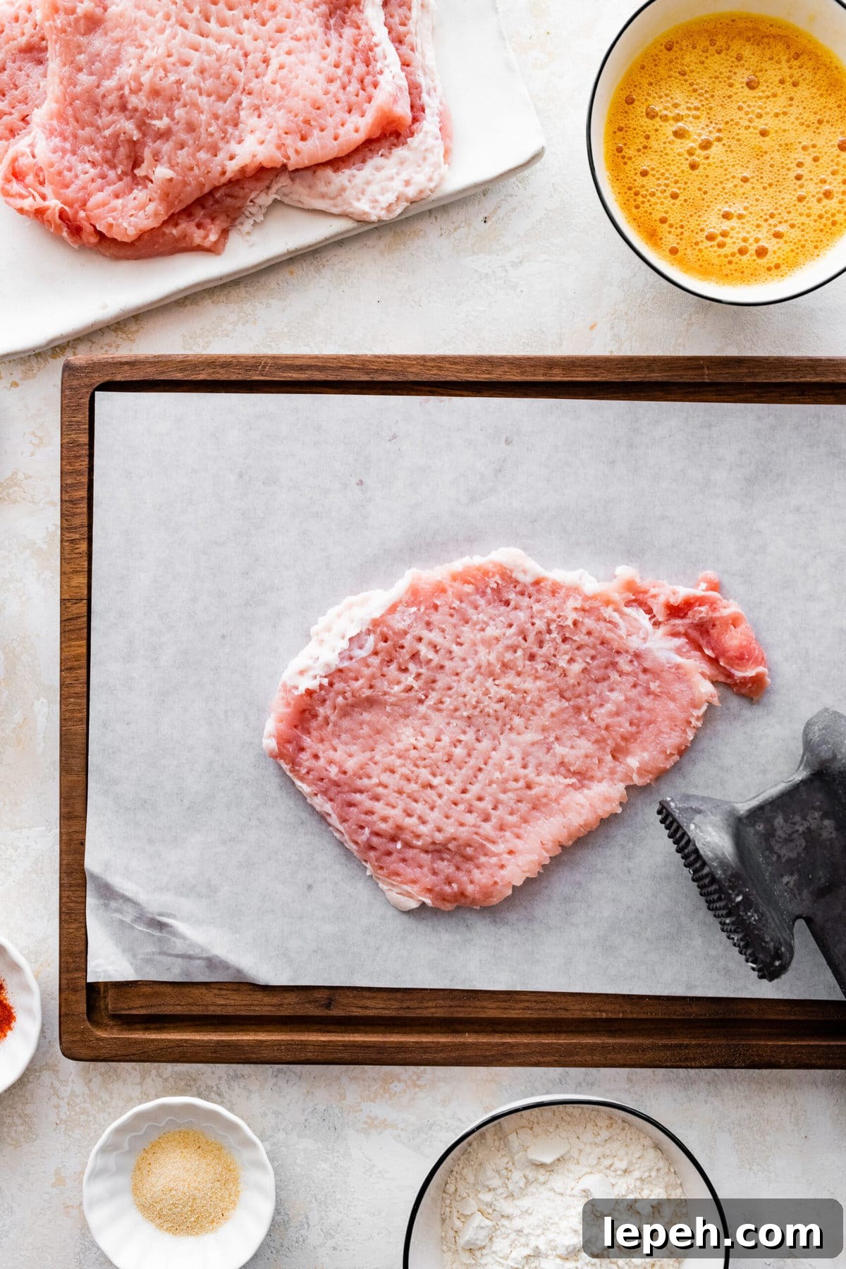 Pounding a pork chop with a meat mallet on a pan.