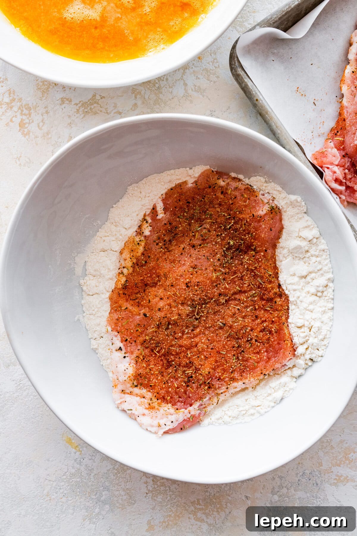 Seasoned pork chop added to a bowl of flour.