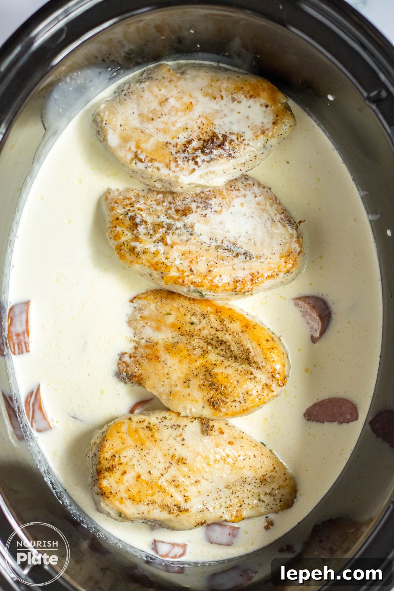 Seared chicken cutlets in a creamy sauce with sliced sausage, all placed in a slow cooker