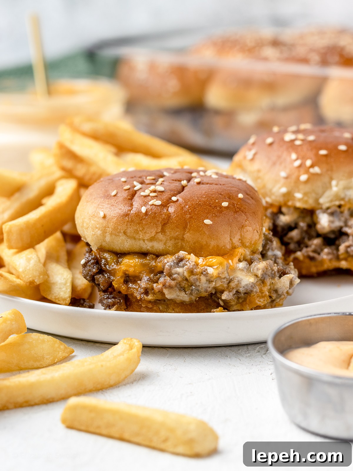 A plate of ground beef cheesy sliders with french fries and sriracha aioli.