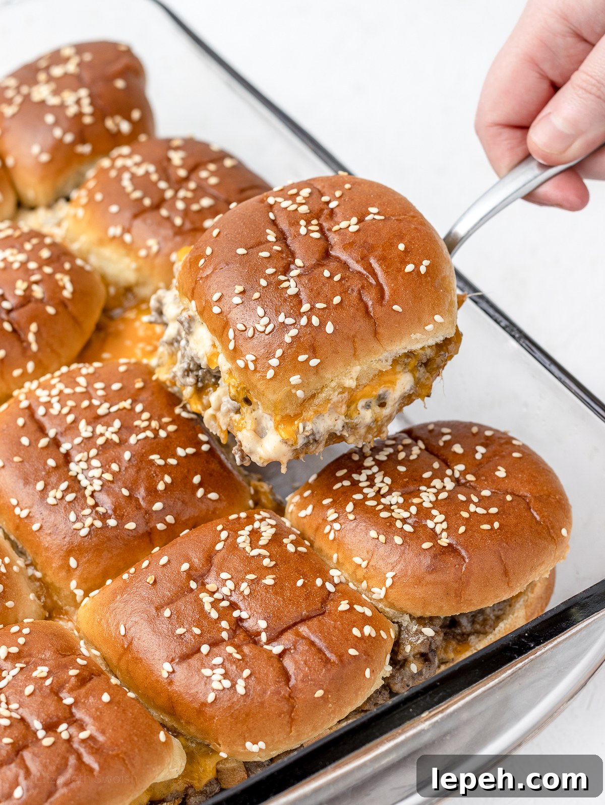 Toasty sliders in a baking pan with a hand lifting one from the pan.