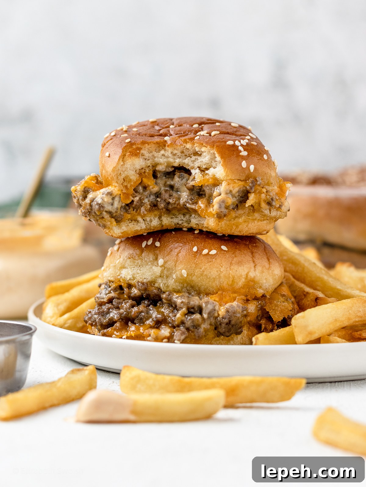 Stack of two ground beef sliders surrounded by french fries and sriracha aioli sauce.