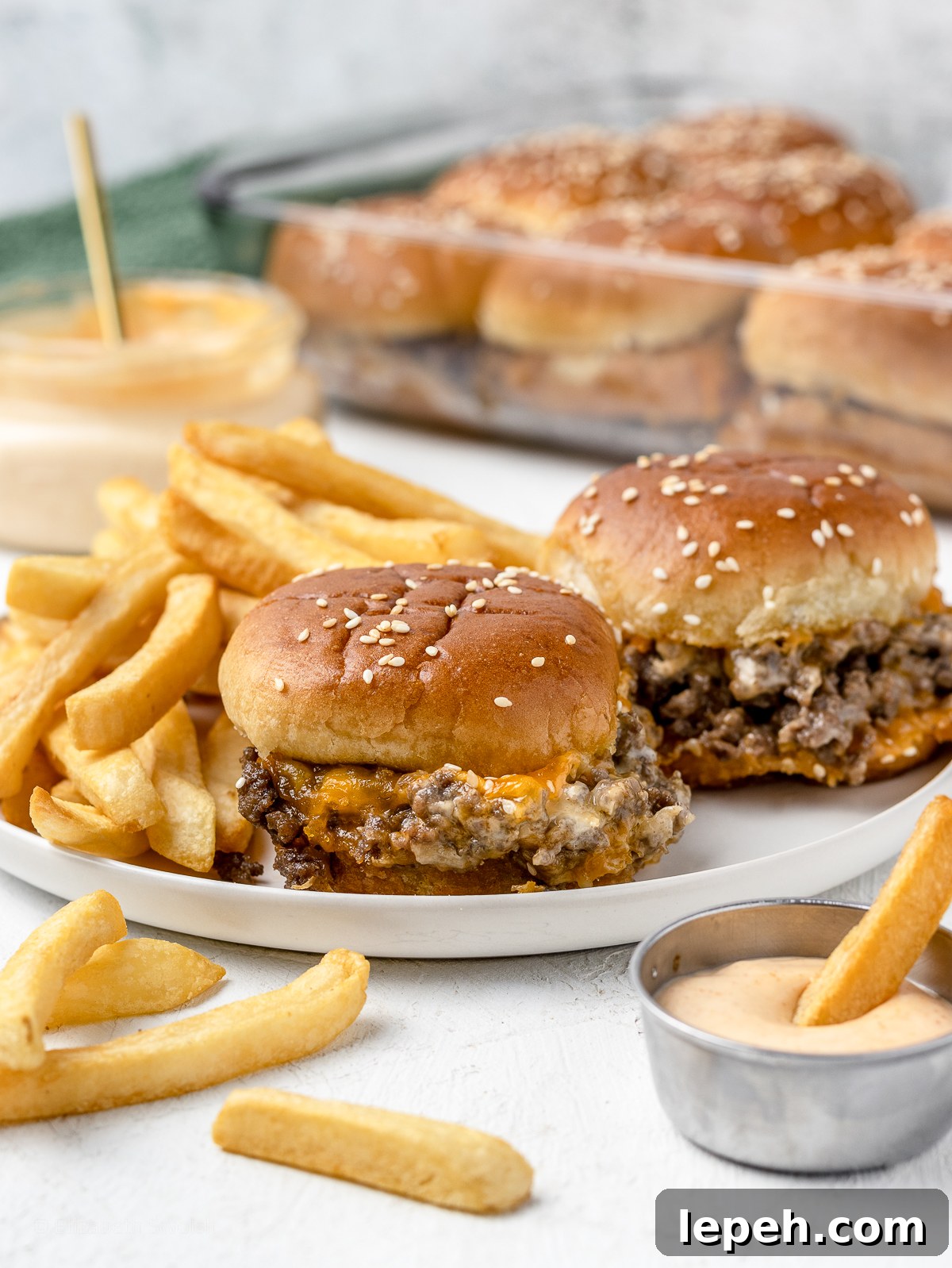 A plate of two cheesy, beefy sliders with fries and sriracha aioli.