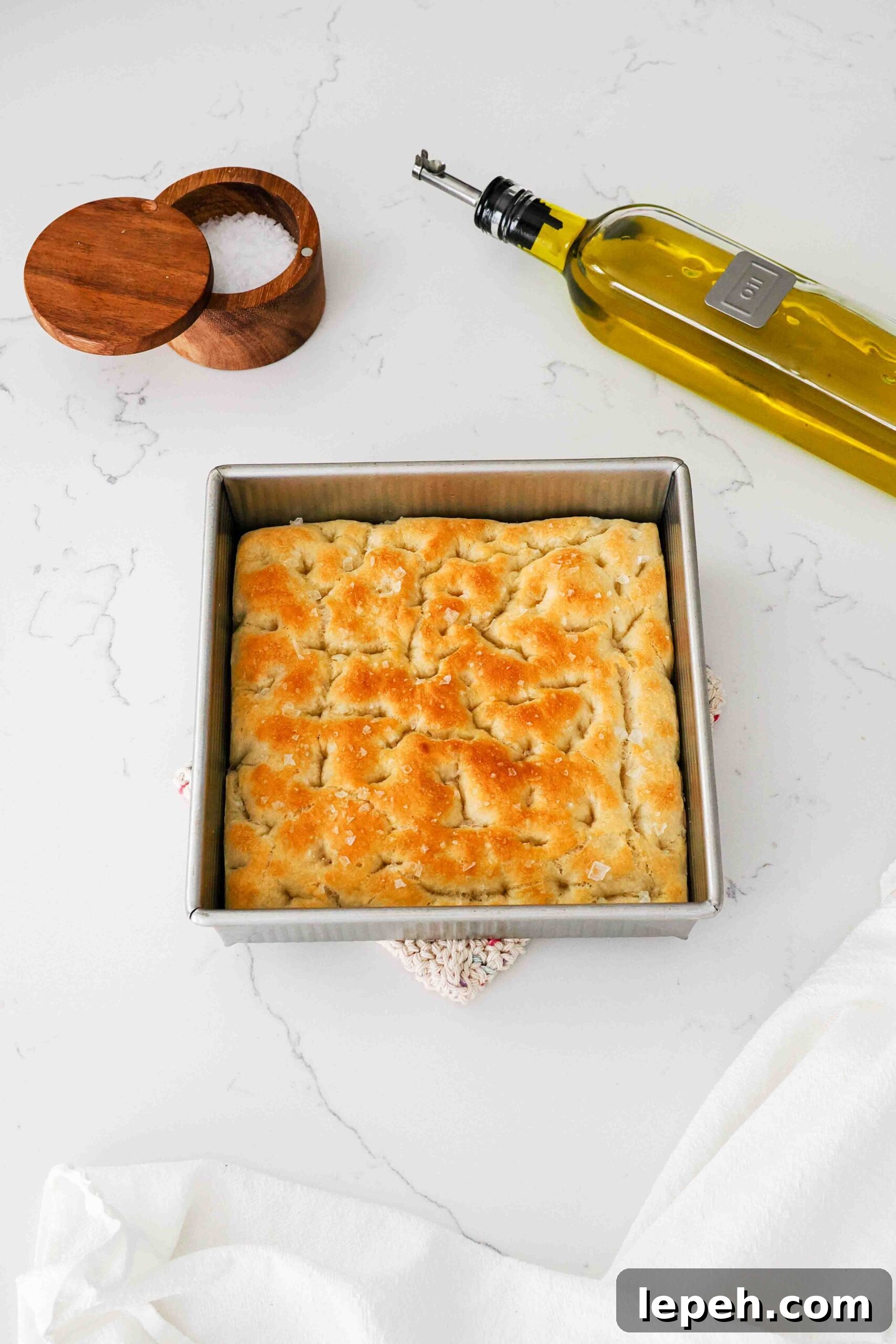 A golden brown loaf of focaccia bread in a square pan on a quartz countertop.