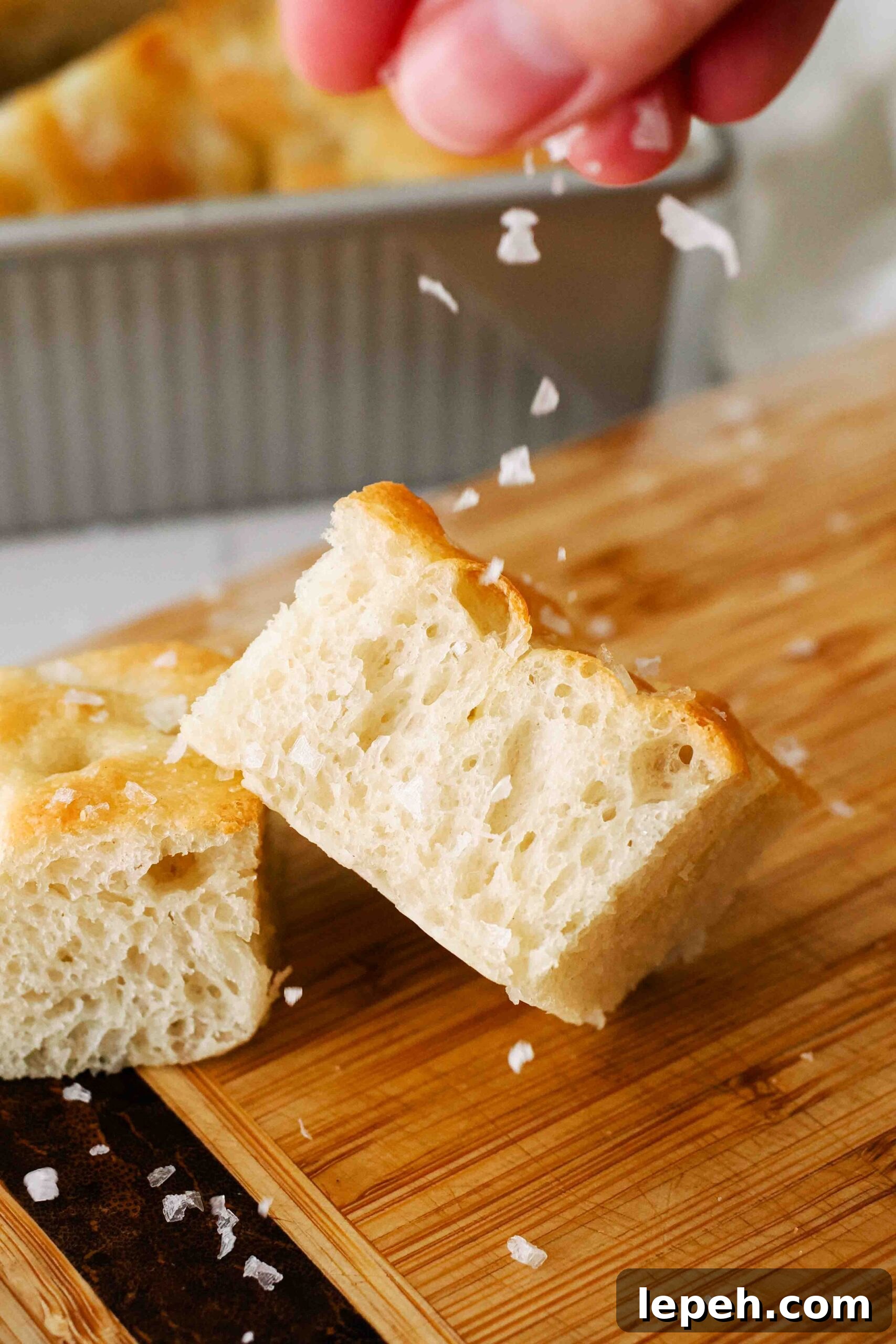 A hand sprinkles salt on top of a slice of focaccia.