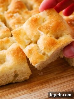 A hand picks up a golden brown square of focaccia bread.