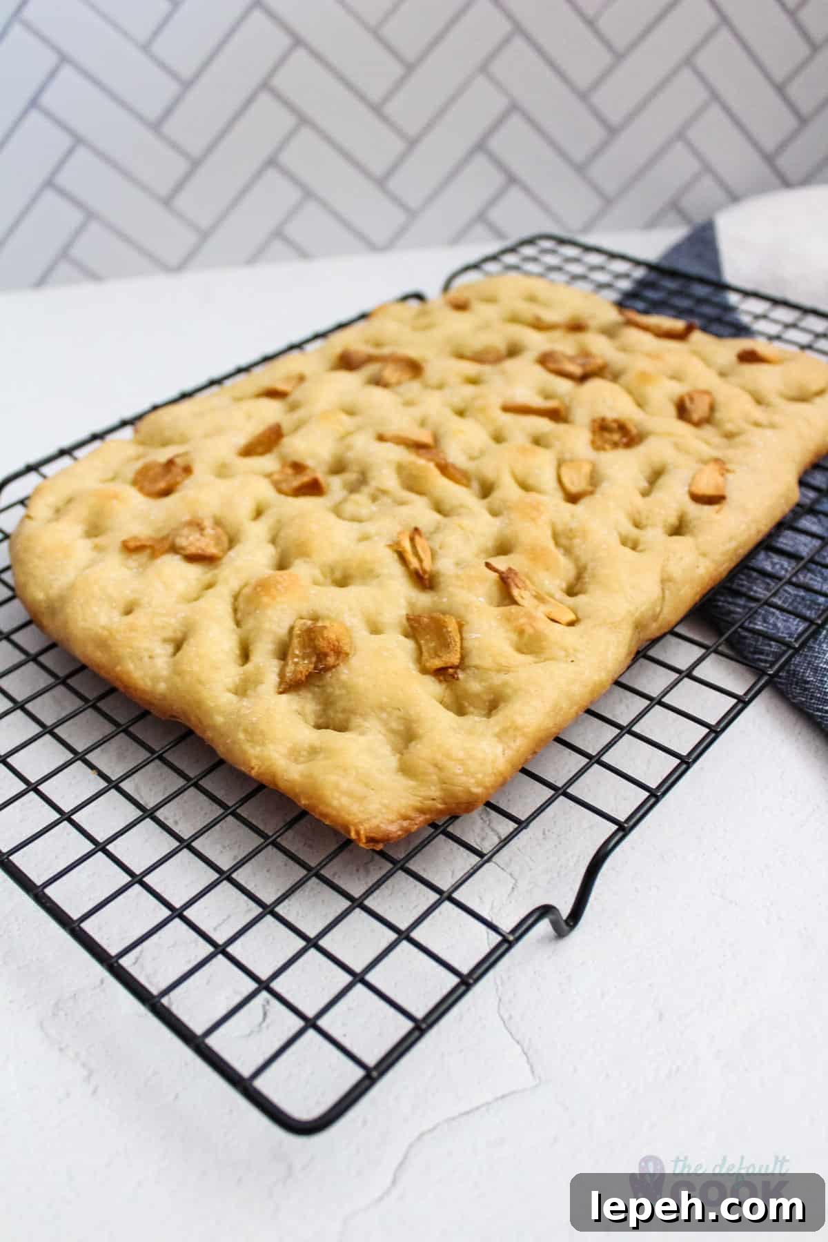Focaccia bread with roasted garlic sitting on a cooling rack on a counter.