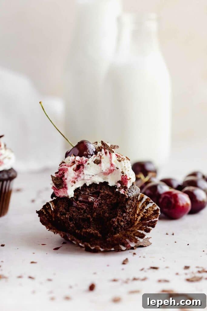 bitten chocolate cupcake with cherry filling, whipped cream, and fresh cherry on top